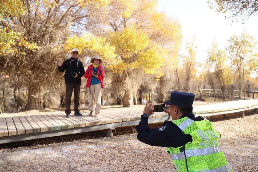 图为库尔勒公安处库车站派出所民警应邀为不雅赏胡杨林搭客拍照打卡。武陇慧摄